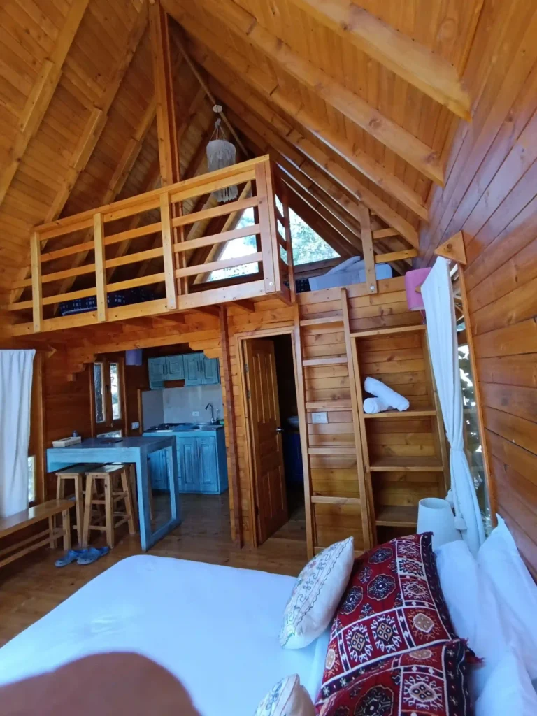 Interior de Cabaña El Ensueño en Villa de Leyva, con decoración rústica de madera, cama, cocina y un loft superior.