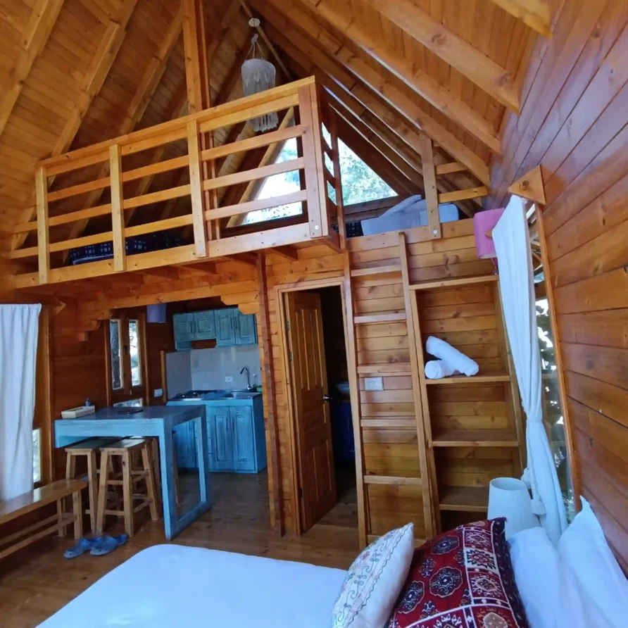 Interior de Cabaña El Ensueño en Villa de Leyva, con decoración rústica de madera, cama, cocina y un loft superior.