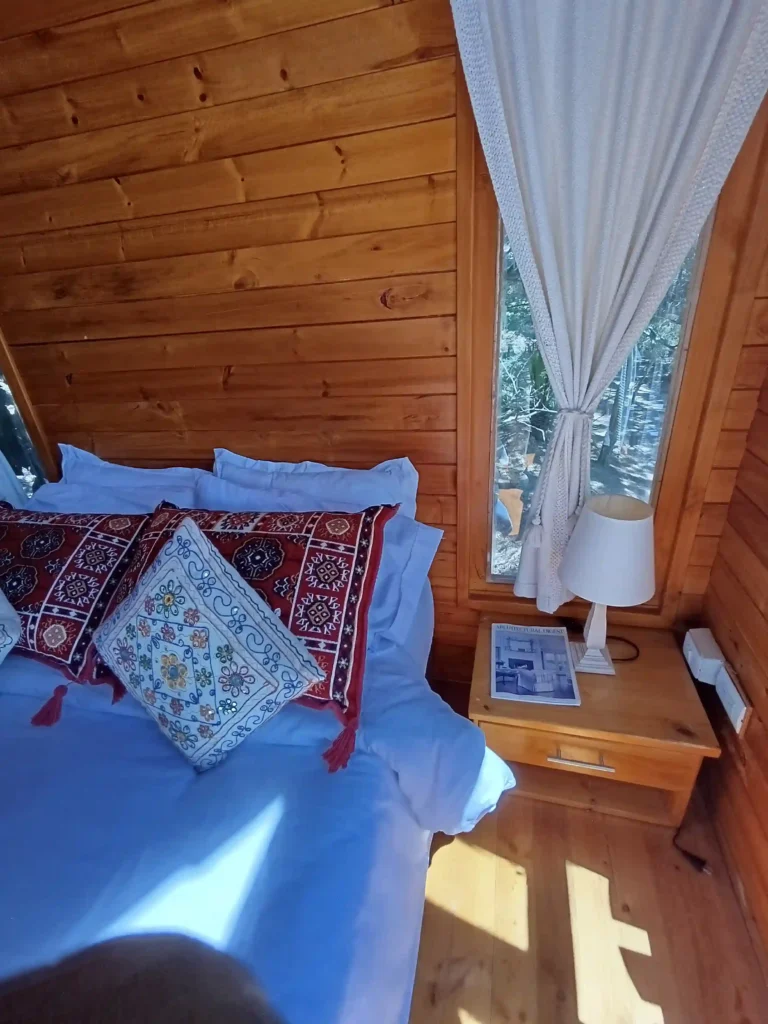 Habitación estilo casa de campo hichatana y zuetana, con mobiliario de pino, textiles decorativos y vistas al exterior. Cabaña el ensueño