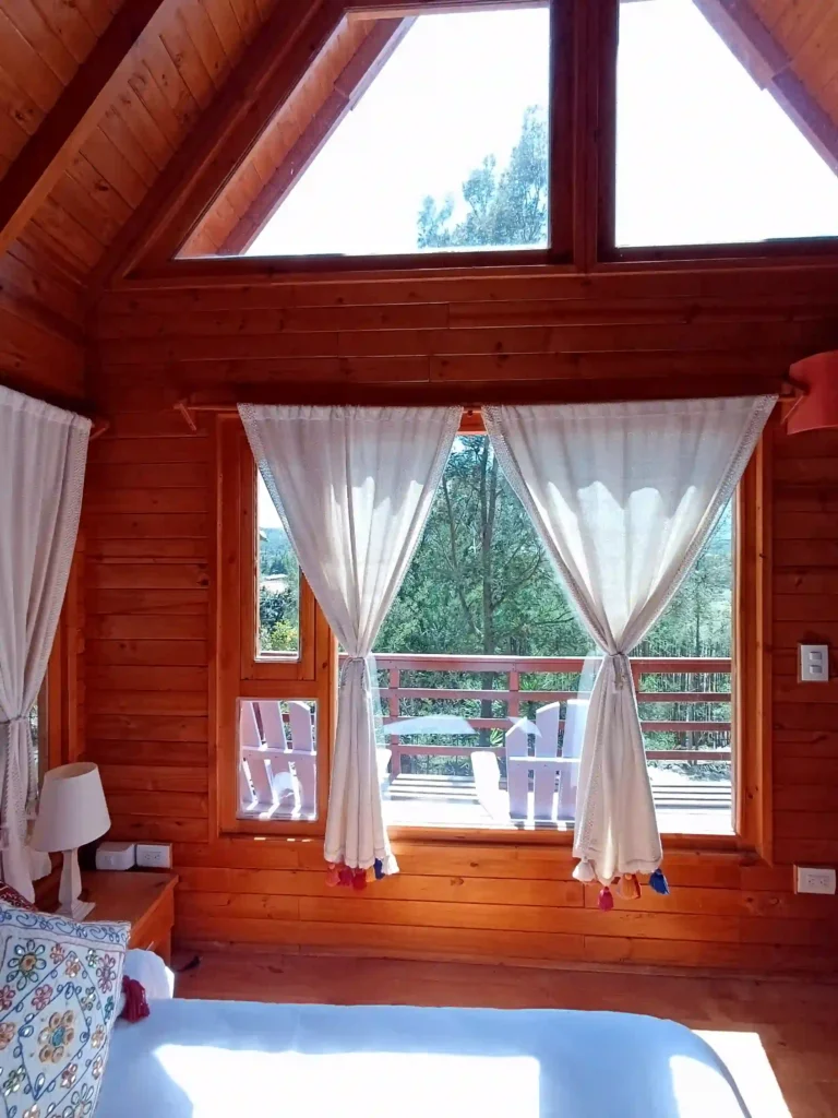 Habitación de Cabaña el Ensueño con paredes de madera, amplios ventanales y vista a un balcón rodeado de bosque.