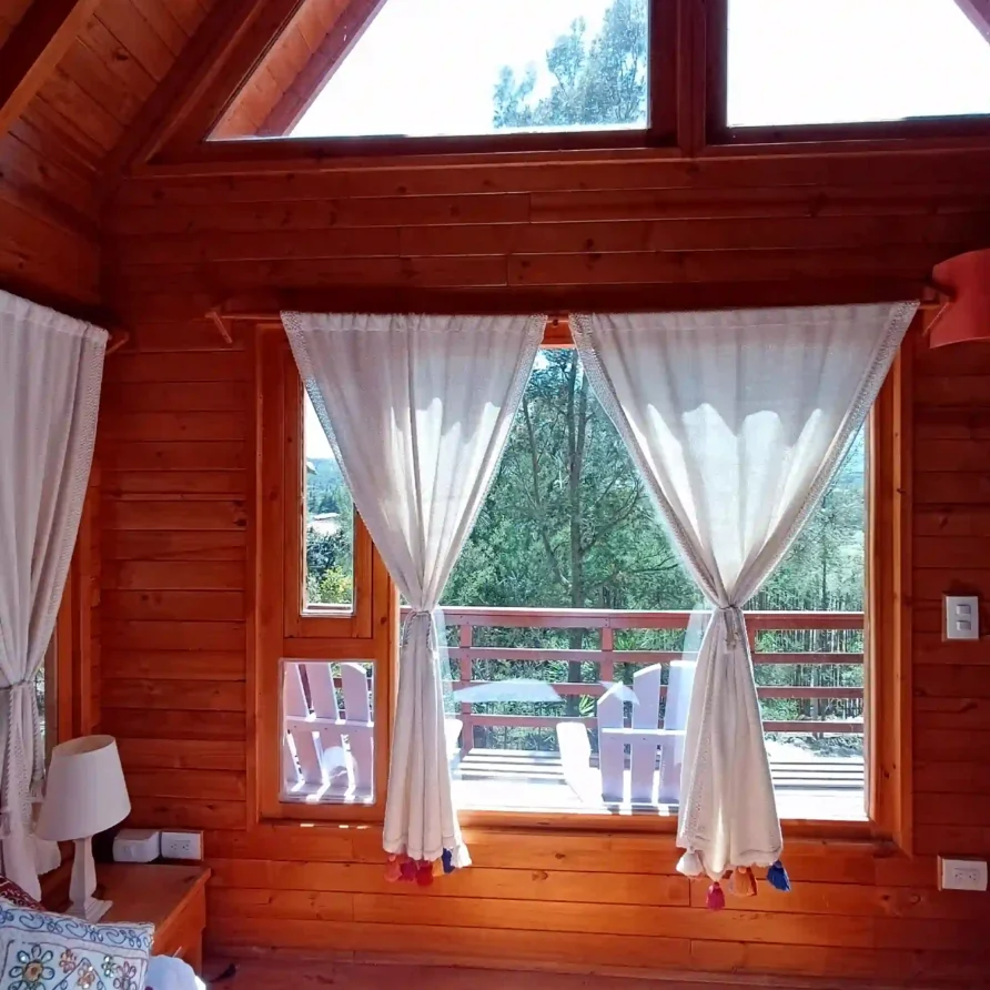 Habitación de Cabaña el Ensueño con paredes de madera, amplios ventanales y vista a un balcón rodeado de bosque.