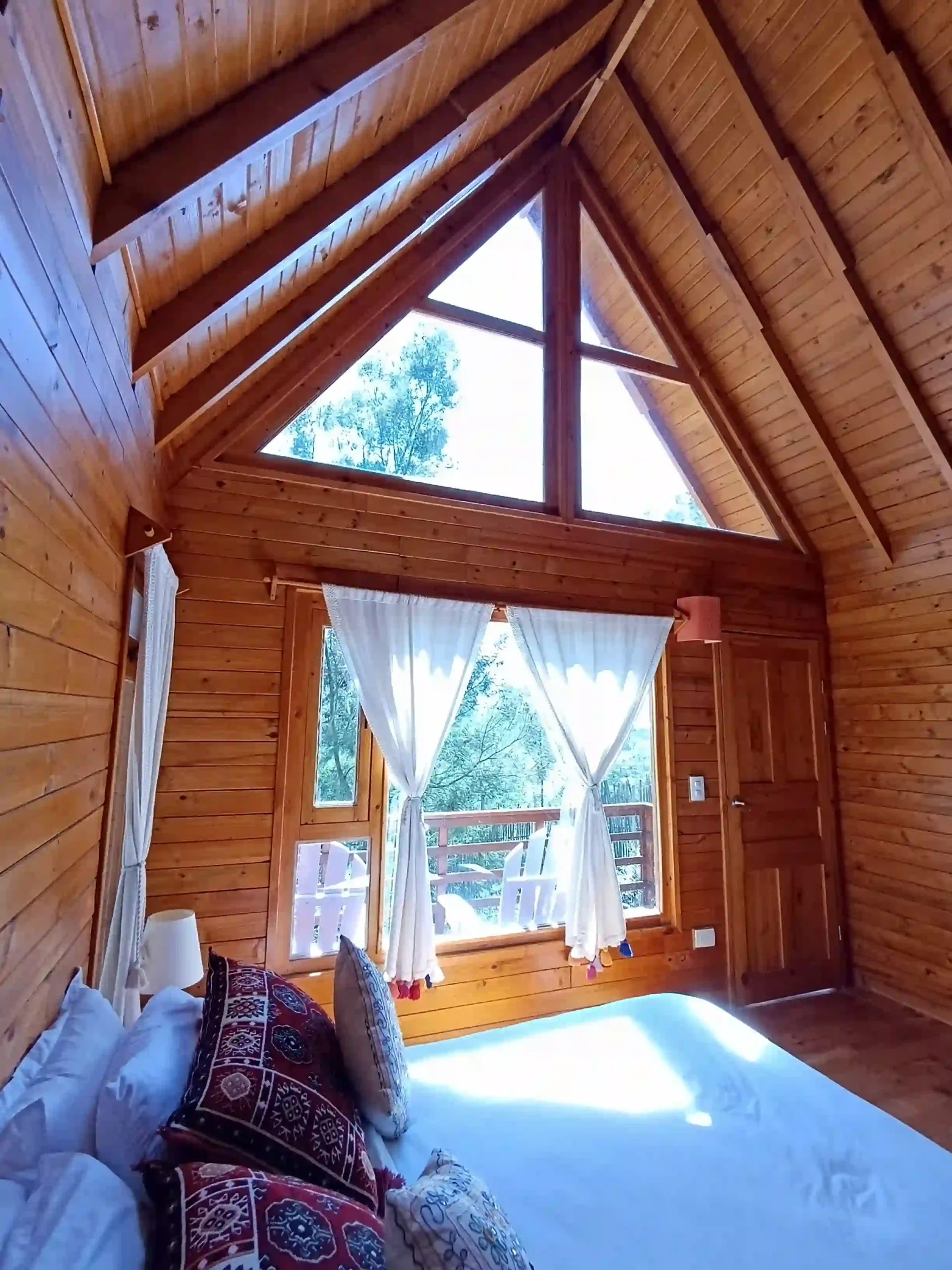 Interior de Cabaña El Ensueño, Villa de Leyva. Dormitorio de madera con ventanales grandes y cama acogedora.