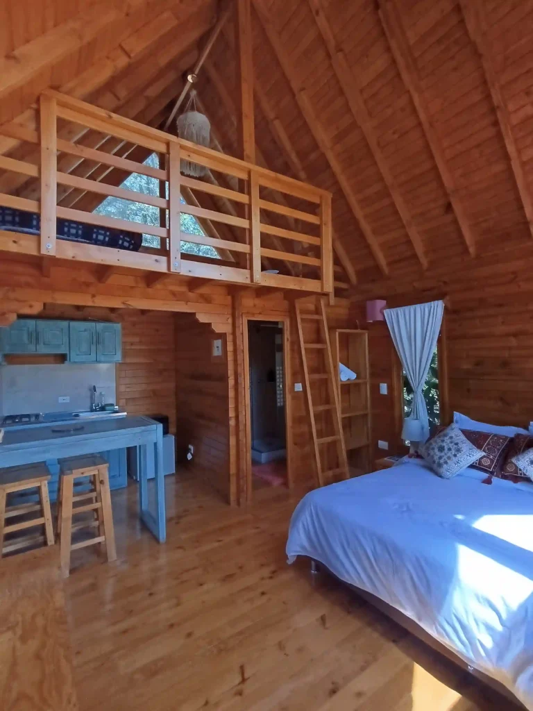 Interior de cabaña de madera 'El Ensueño' con cama, cocina y altillo, ideal para hospedaje premium en Villa de Leyva.