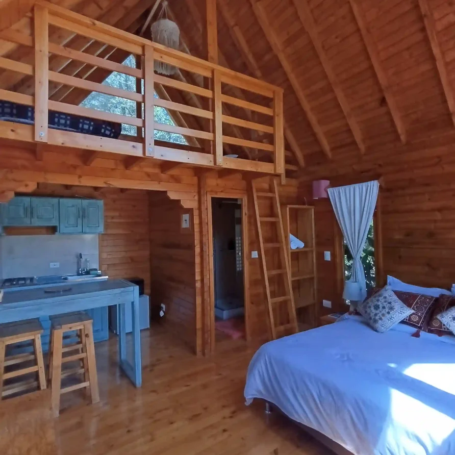 Interior de cabaña de madera 'El Ensueño' con cama, cocina y altillo, ideal para hospedaje premium en Villa de Leyva.