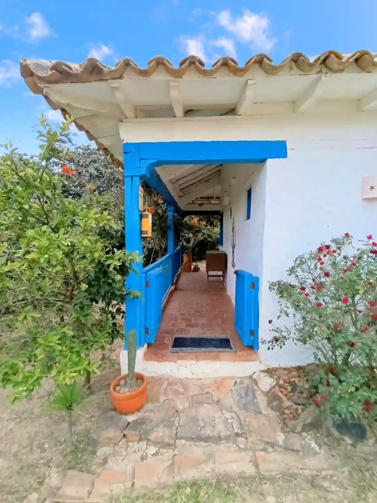 Entrada principal de una casa de campo premium en Villa de Leyva, con balcón azul y camino de ladrillo.