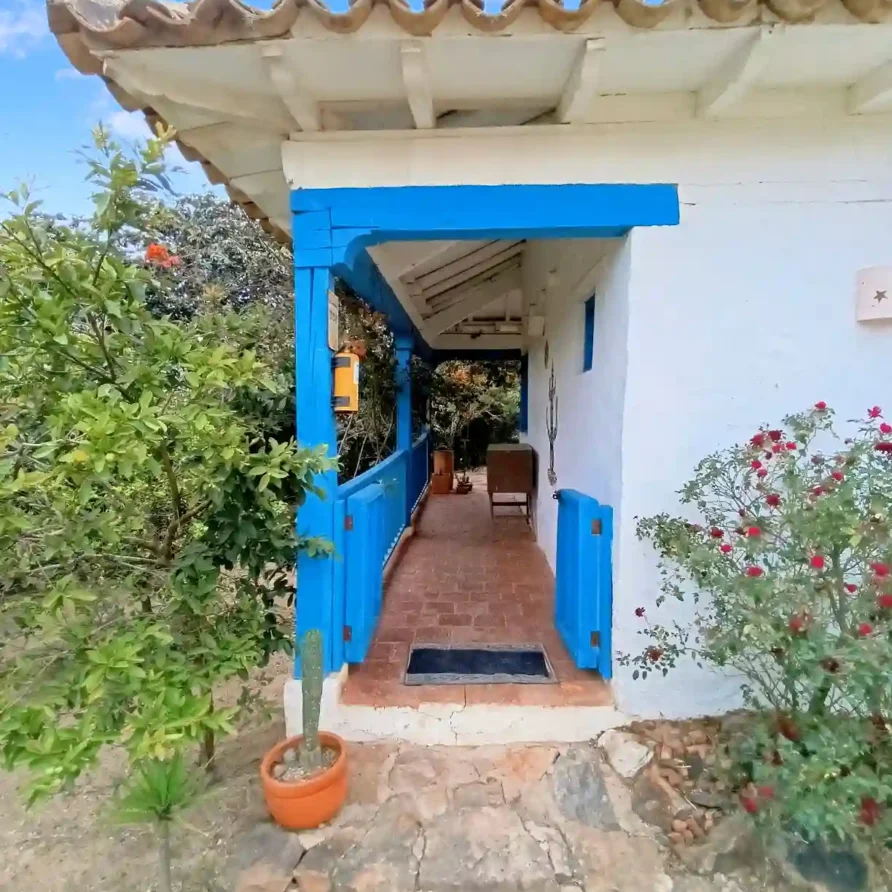 Entrada principal de una casa de campo premium en Villa de Leyva, con balcón azul y camino de ladrillo.