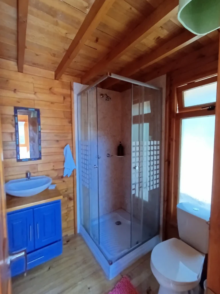 Interior de baño en Cabaña El Ensueño, estilo rústico moderno, con ducha, lavamanos azul y acabados de madera.