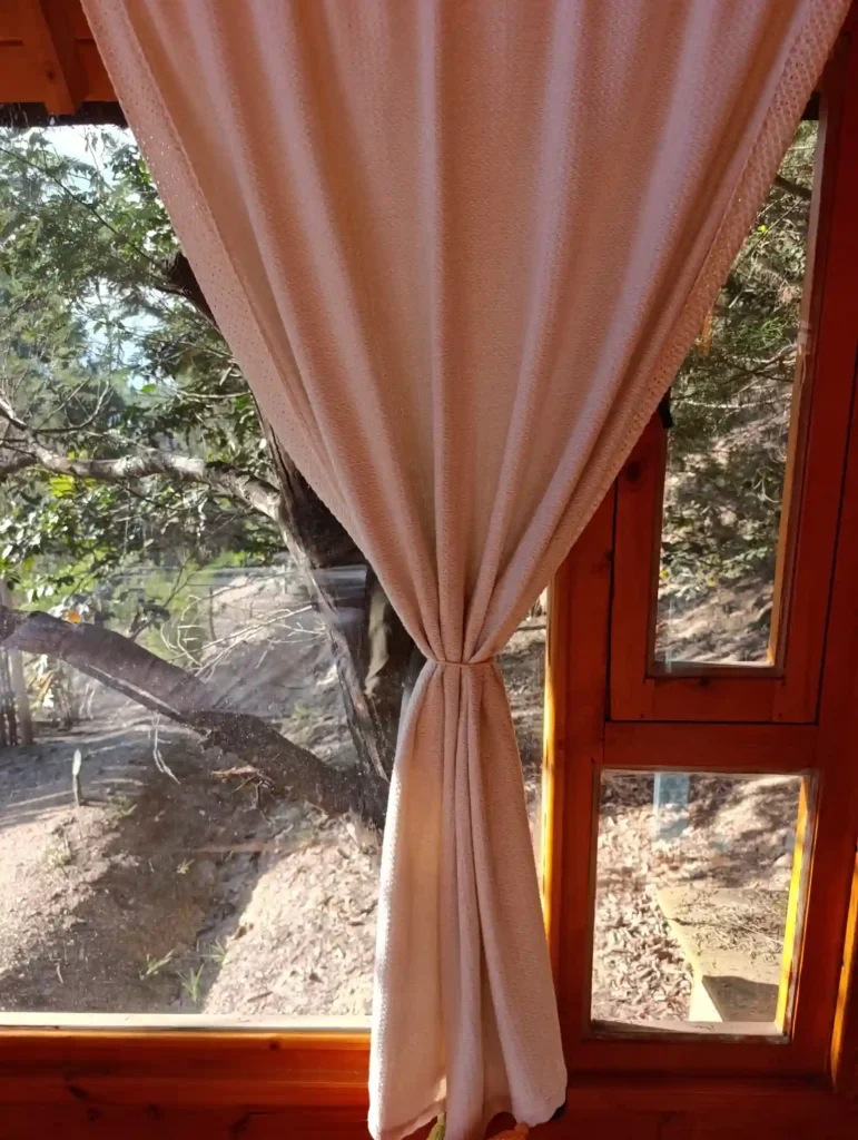 Cortina beige atada en ventana de madera, mostrando vista natural exterior de cabaña el ensueño o casa de campo en villa del leyba