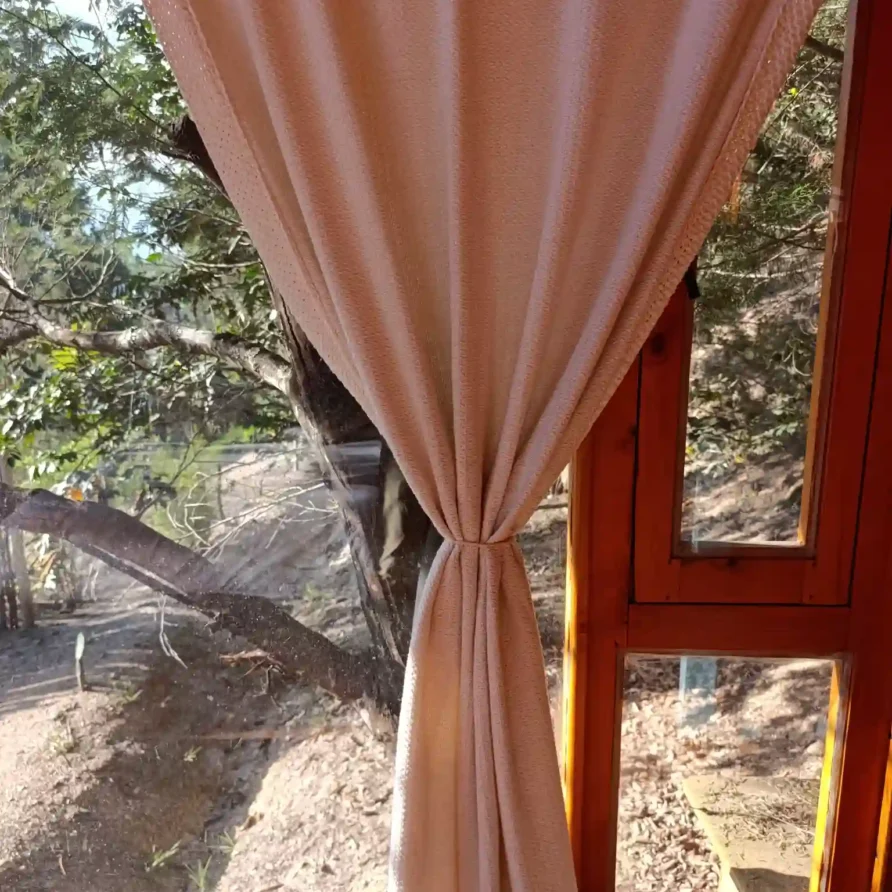 Cortina beige atada en ventana de madera, mostrando vista natural exterior de cabaña el ensueño o casa de campo en villa del leyba