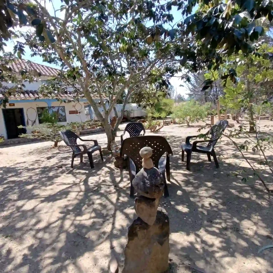 Área exterior sombreada de cabaña en Villa de Leyva con mesa y sillas, y un cairn de piedras.