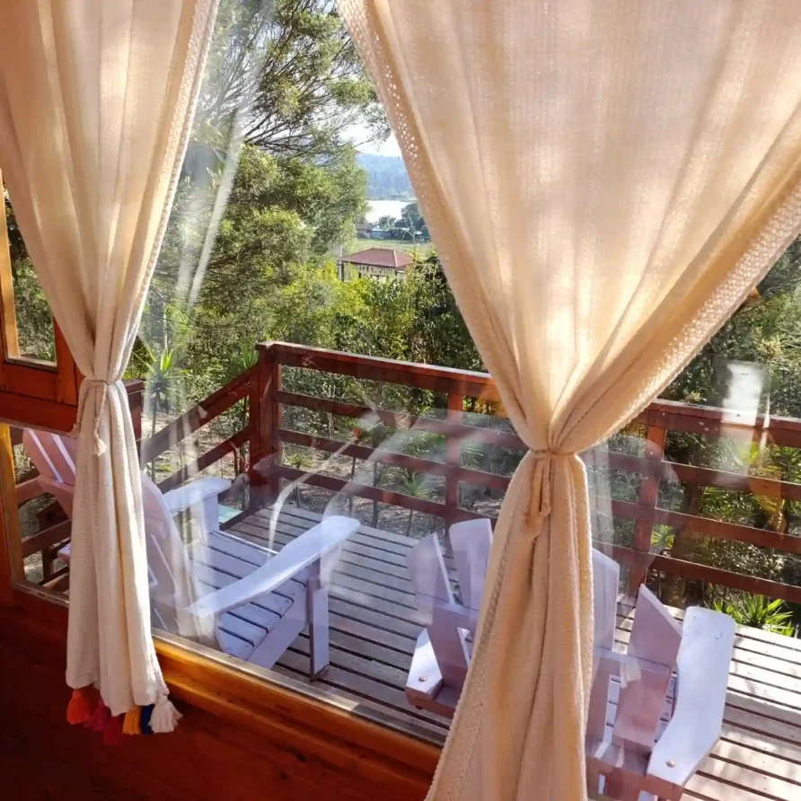 Ventana de cabaña el ensueño en Vereda Monquirá con cortinas claras y panorámica a balcón de madera y entorno natural.