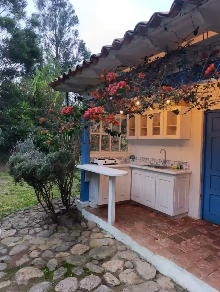 Cocina exterior rústica en cabaña premium de Villa de Leyva con gabinetes blancos, patio de piedra y buganvillas.