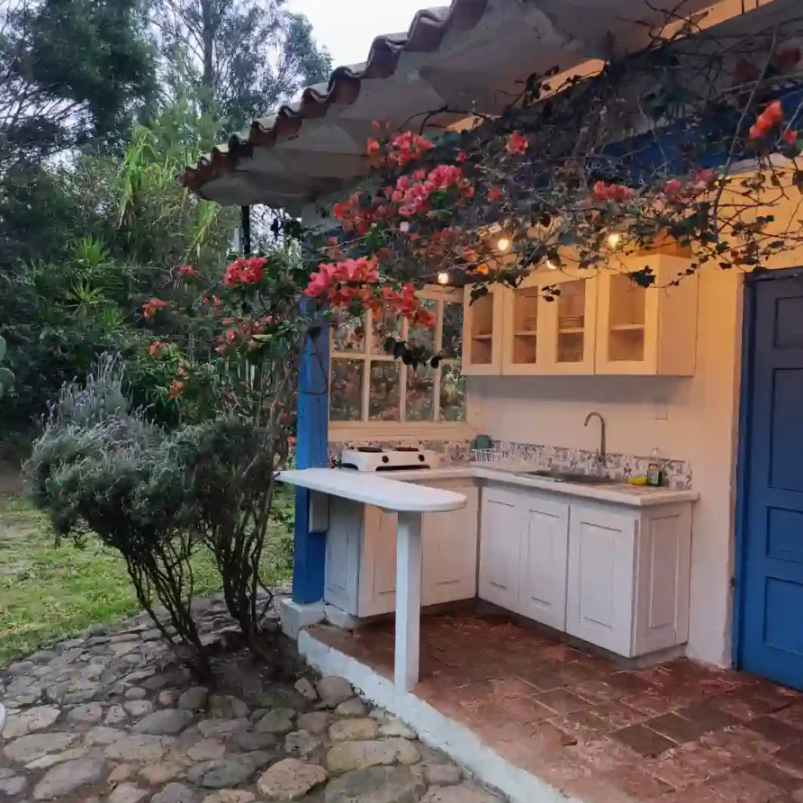 Cocina exterior rústica en cabaña premium de Villa de Leyva con gabinetes blancos, patio de piedra y buganvillas.