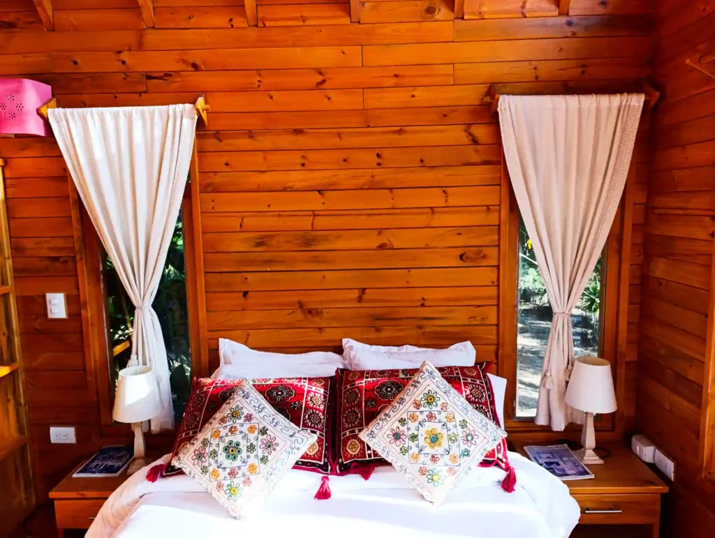 Dormitorio acogedor de Cabaña el Ensueño con paredes de madera, cama premium y almohadas bordadas en Villa de Leyva.