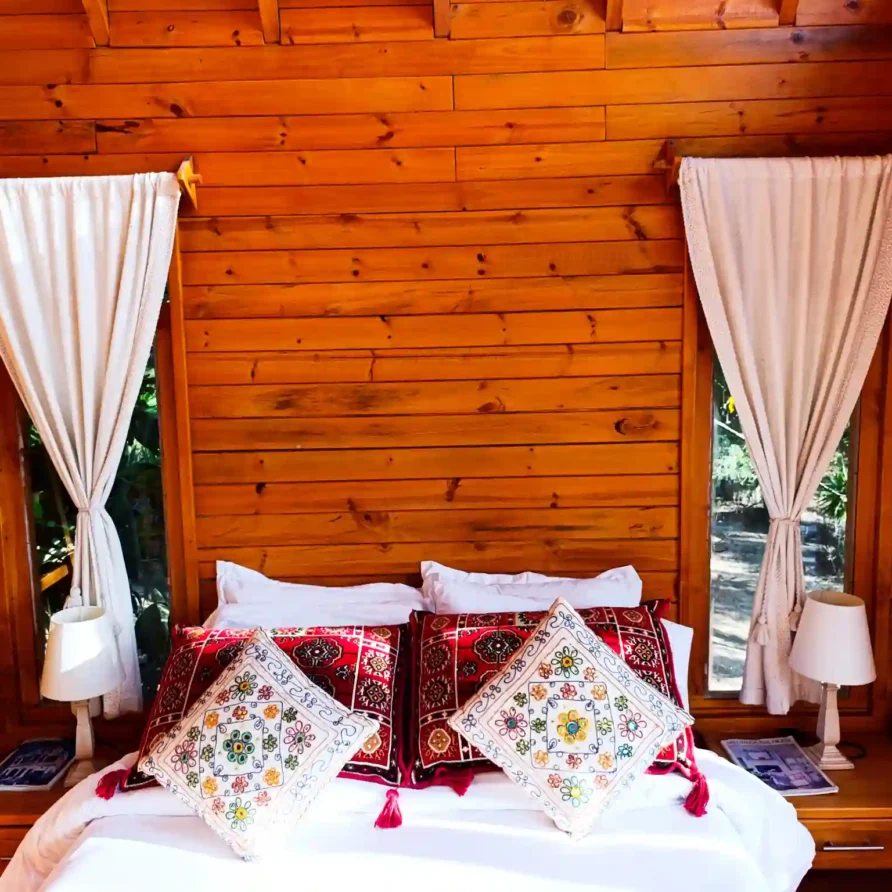 Dormitorio acogedor de Cabaña el Ensueño con paredes de madera, cama premium y almohadas bordadas en Villa de Leyva.