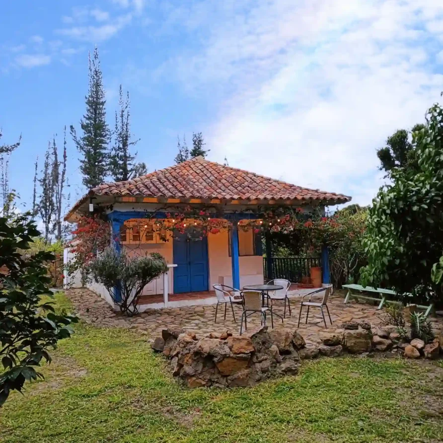 Cabaña El Oteo, Villa de Leyva. Casa de campo con patio, jardín, flores y puertas azules, ideal para hospedaje rural.