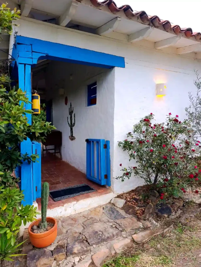 Cabaña premium en Villa de Leyva: entrada acogedora, fachada blanca, detalles en azul y vegetación vibrante.