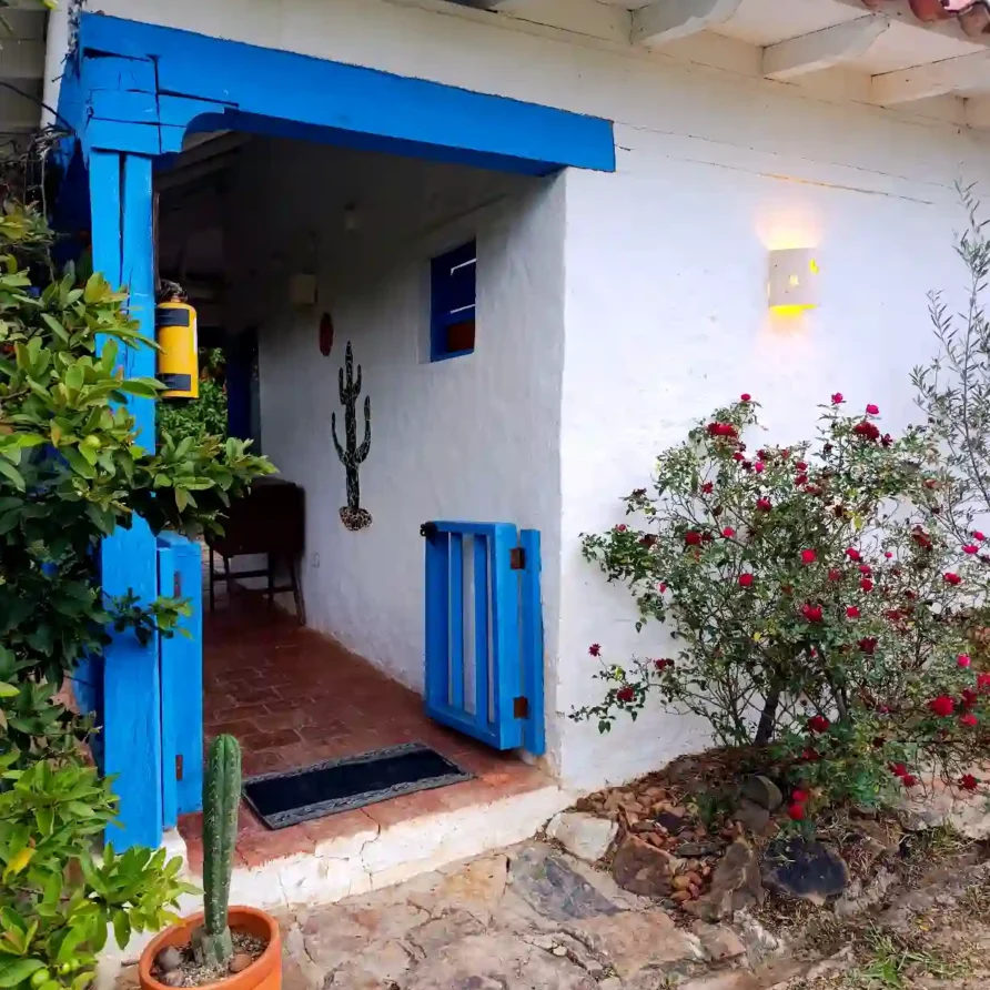 Cabaña premium en Villa de Leyva: entrada acogedora, fachada blanca, detalles en azul y vegetación vibrante.
