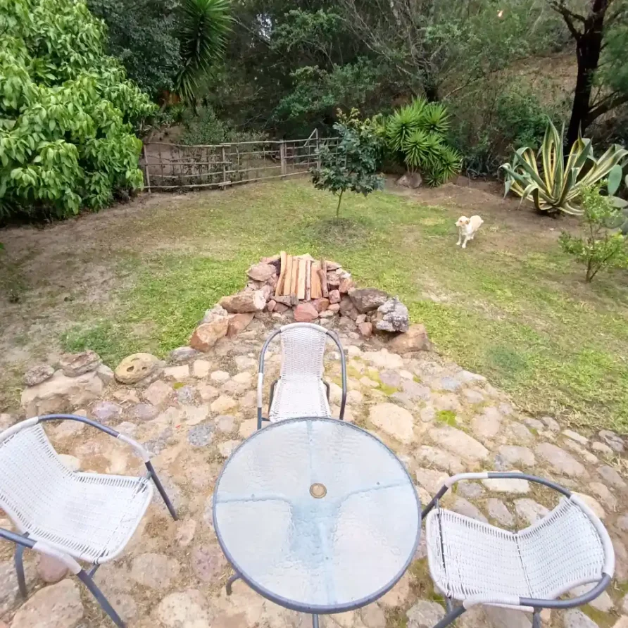 Jardín de Cabaña El Oteo en Villa de Leyva con patio de piedra, mesa, sillas, fogata y vegetación natural.
