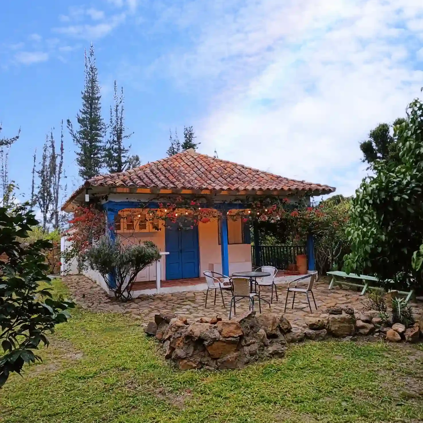 Cabaña El Oteo, Villa de Leyva. Casa de campo con patio, jardín, flores y puertas azules, ideal para hospedaje rural.