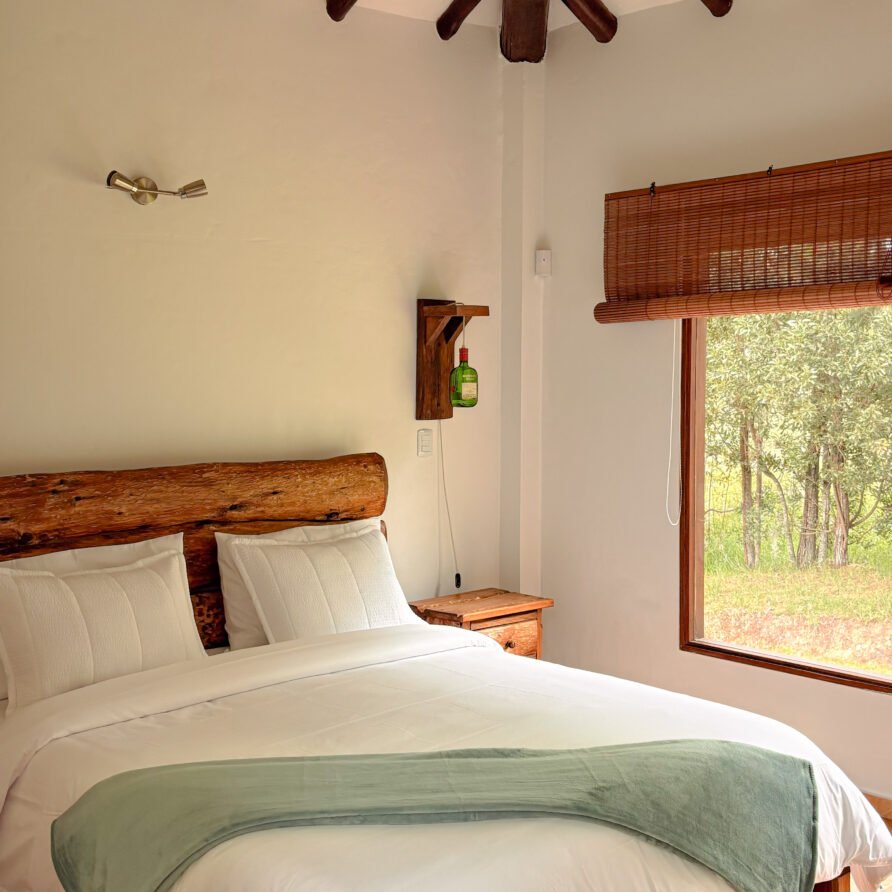 Interior de casa Hichatana: cama con cabecero de madera y techo con vigas.